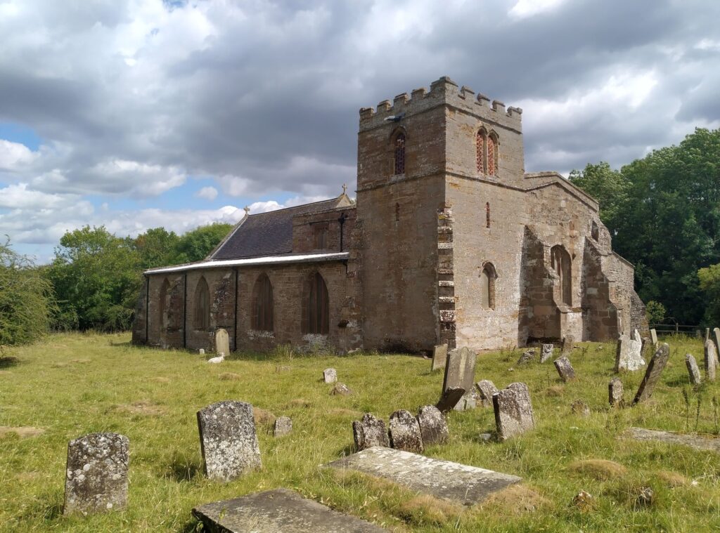 Colour photograph of the outside of a medieval church with a square tower.