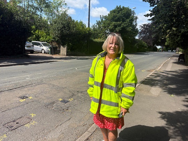 Photograph of Cllr Hetherton in hi viz standing in front of a road awaiting repairs.