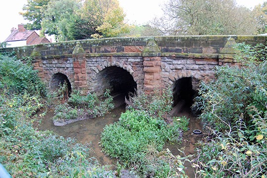 Colour photo of a three arched stone bridge with a river flowing underneath