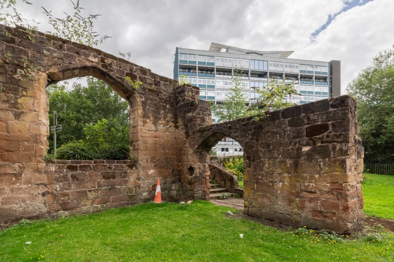 Colour photo showing stone remains, with a block of flats behind.