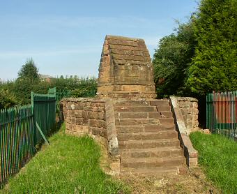 Colour photo of a stone well with steps up to a plinth.