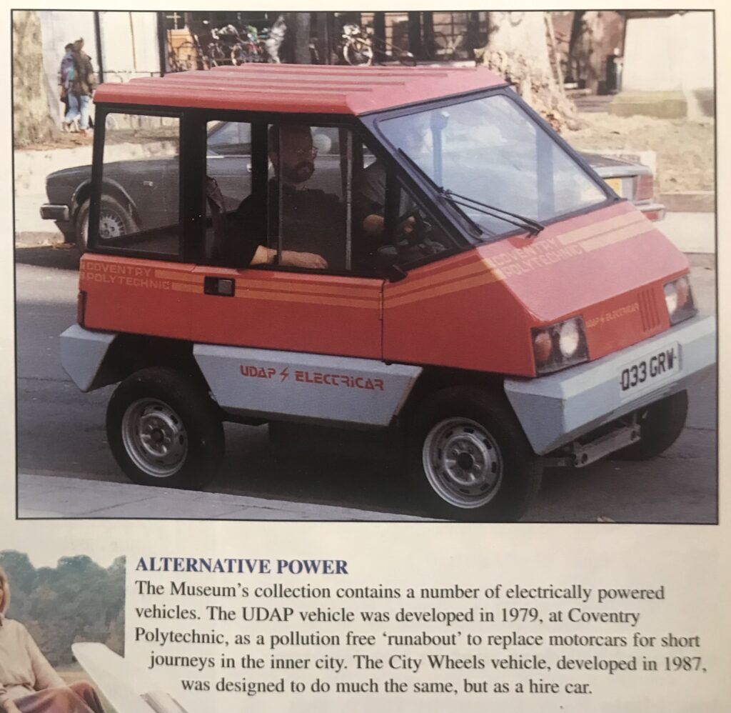A small red-and-grey electric car labeled “UDAP Electricar” from Coventry Polytechnic, with a driver seated inside, parked on a street.