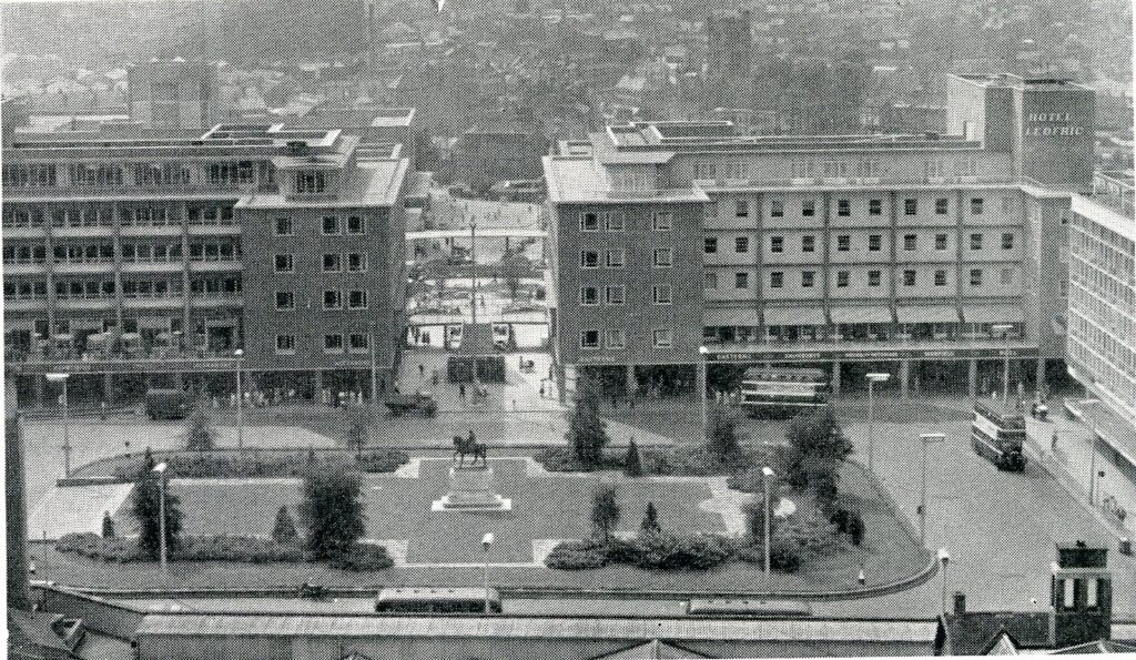 Monochrome photograph of Broadgate, Coventry, showing a statue of Lady Godiva in the centre, surrounded by greenery with buildings behind.