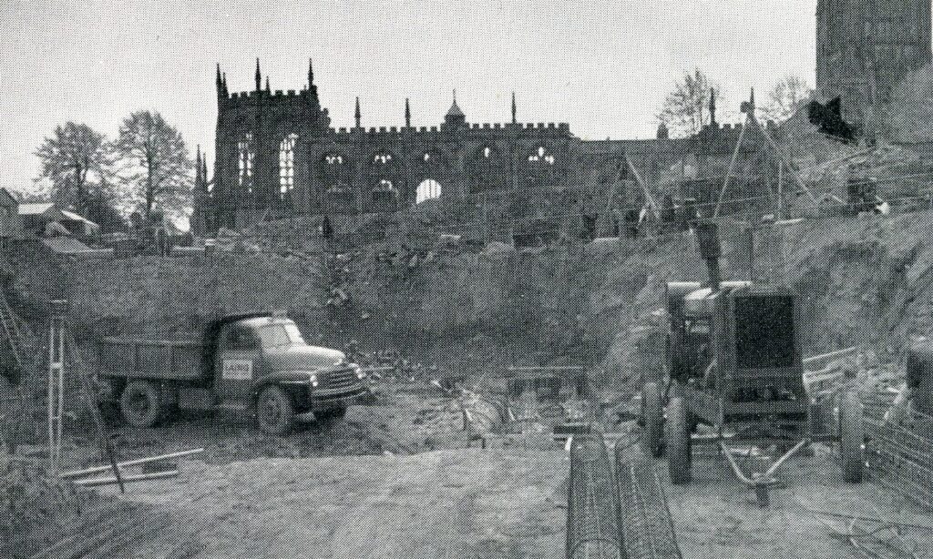 Monochrome photograph showing the remails of the old cathedral in the background and a lorry and machine in a hollow in the foreground.
