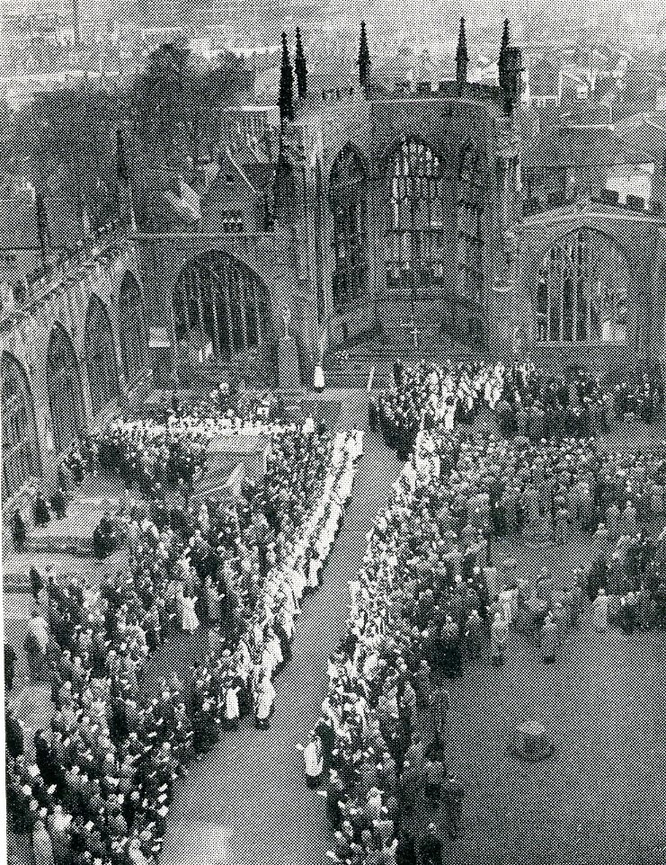 Monochrome photograph of the ruins of Coventry Cathedral crowded with people with clergy in two lines.