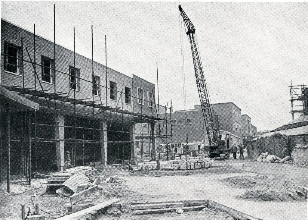 Monochrome photograph of a building site, with a crane. 