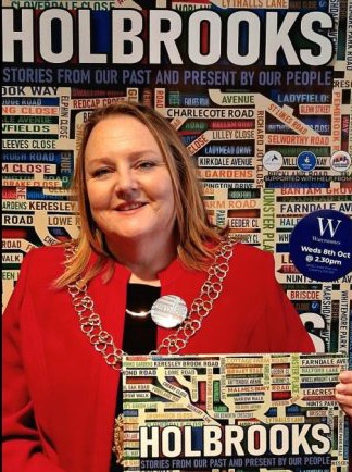 Photograph of Rachel Lancaster in front of an image of the Holbrooks book and holding a coy of the book.
