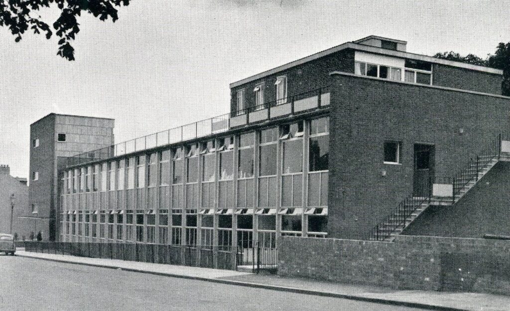 Monochrome photograph showing a modern building facing a road.